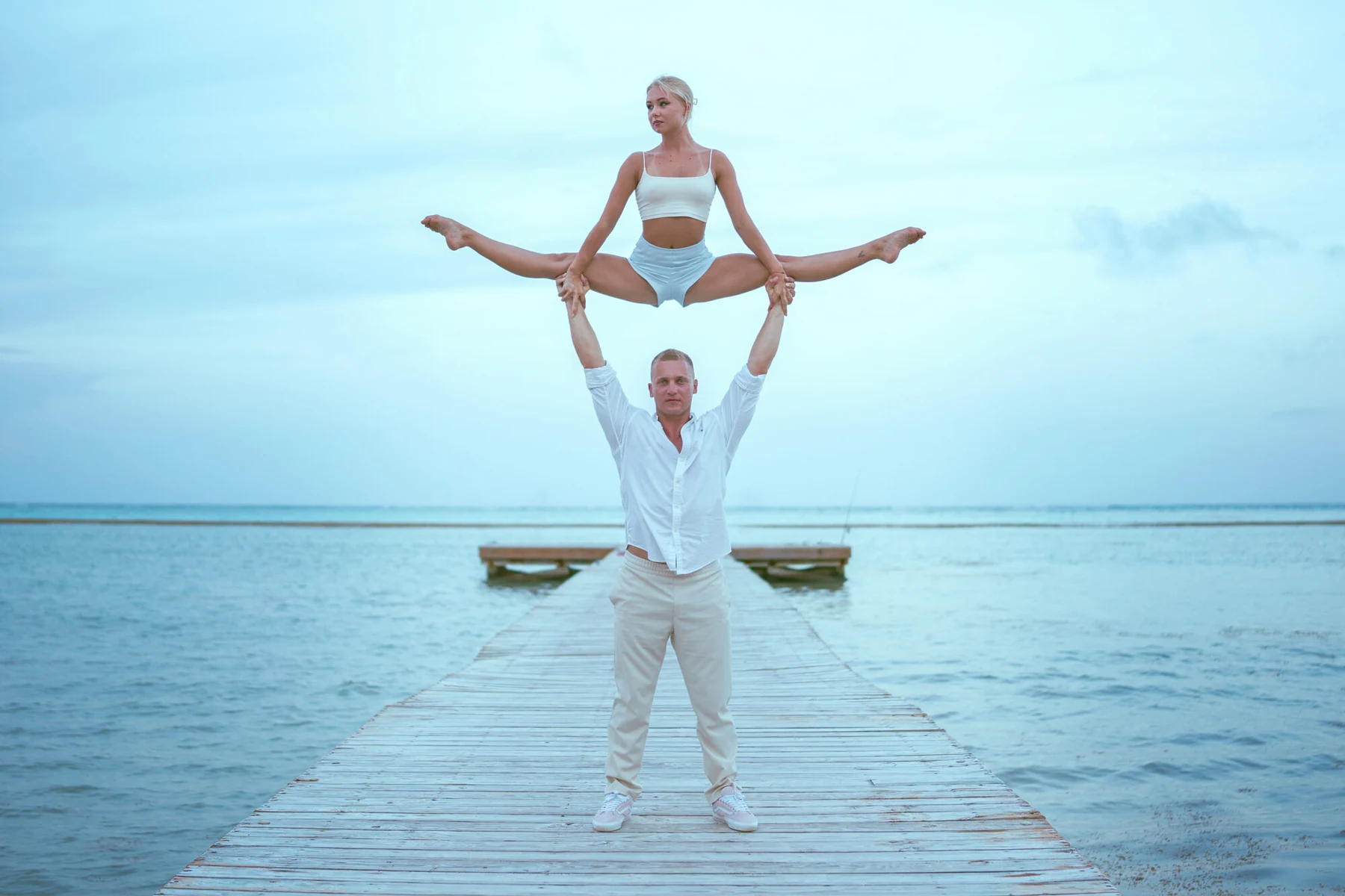 The duo balancing in white costumes beside the sea
